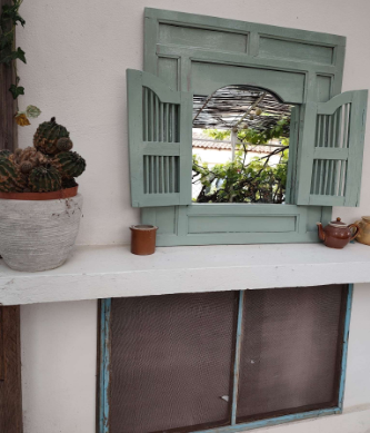 Miroir décoratif en forme de fenêtre à volets verts et cactus en pot en terrasse extérieure à la Maison Oyat's Mer au Grau-du-Roi